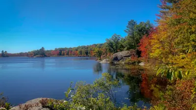 Autumn foliage surrounding a serene lake under a clear blue sky.