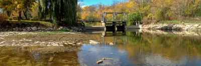 A view of a river with low water at the foreground, leading to a small dam at the center.