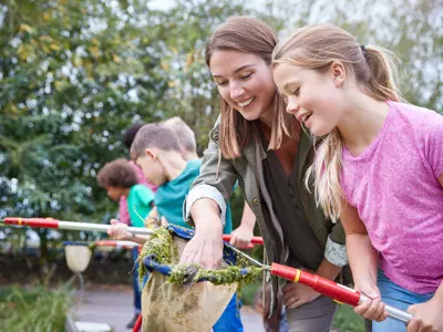 An adult and a child engaging in outdoor environmental conservation activities, using nets to collect samples from a pond.
