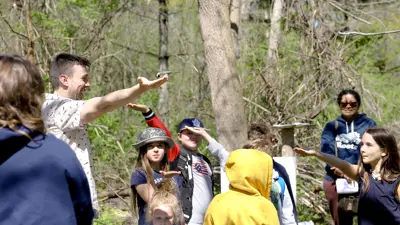 A group of children and adults participating in an outdoor educational activity in a forested area.