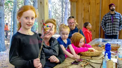 A group of people participating in a craft workshop at a wooden table in a forest setting.