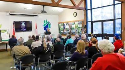 A person speaking at a podium in a meeting room filled with attendees facing them. 