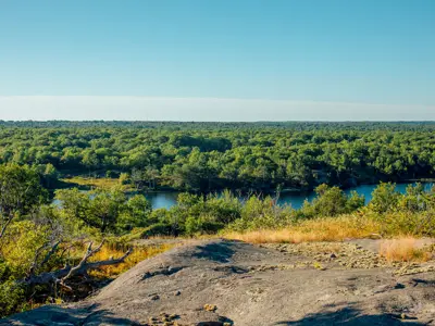 A scenic view of Sheffield Conservation Area featuring a vast expanse of lush greenery surrounding a serene blue lake, with rocky terrain in the foreground under clear blue skies.