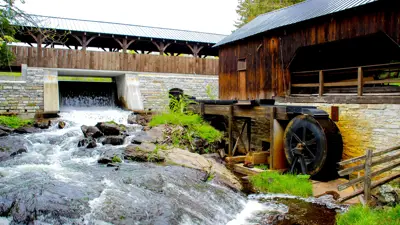 View of O'Hara Mill, featuring a historic wooden mill with a water wheel beside a flowing stream and a covered bridge in the background.