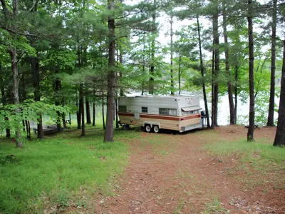 An old RV parked among trees next to a serene lake.