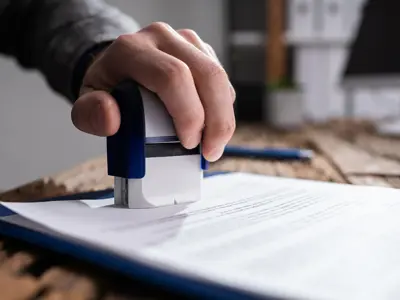 A person using a stamp on a document placed on a clipboard on a wooden desk.