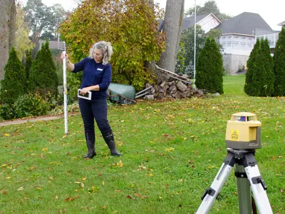 A person using surveying instrument on a tripod in a residential yard.