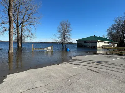 Flooded park area with standing water surrounding trees and a picnic table, reaching up to a building.